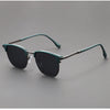 A pair of dark green classic square metal frame sunglasses resting on a gray surface.