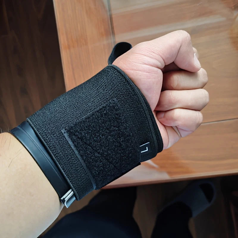 Une main porte un bandeau ajustable noir pour l'entraînement de force sur une surface en bois.