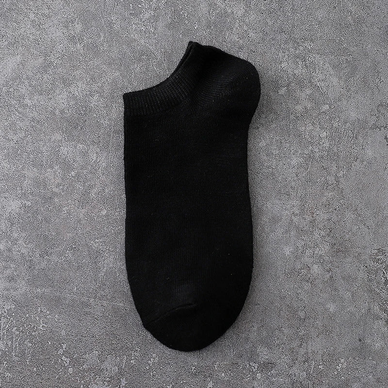 A black ankle sock lying flat on a gray textured surface.