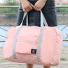 A person is holding a light pink foldable travel duffel bag with gray straps outdoors.