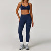 A woman wearing a navy blue 3-piece yoga sports set consisting of a cropped top, leggings, and a sports bra.