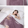 A woman wearing a purple fleece bath robe is relaxing on a bed.