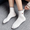 Pair of white yoga socks with brown embroidery on the cuff and toe, displayed on a gray surface.