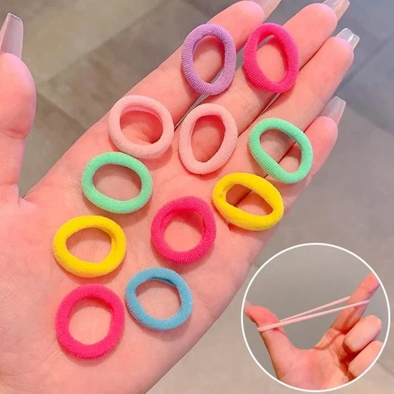 Eine Hand zeigt verschiedene bunte Nylon-Elastikhaarspangen in rosa, lila, grün und gelb.