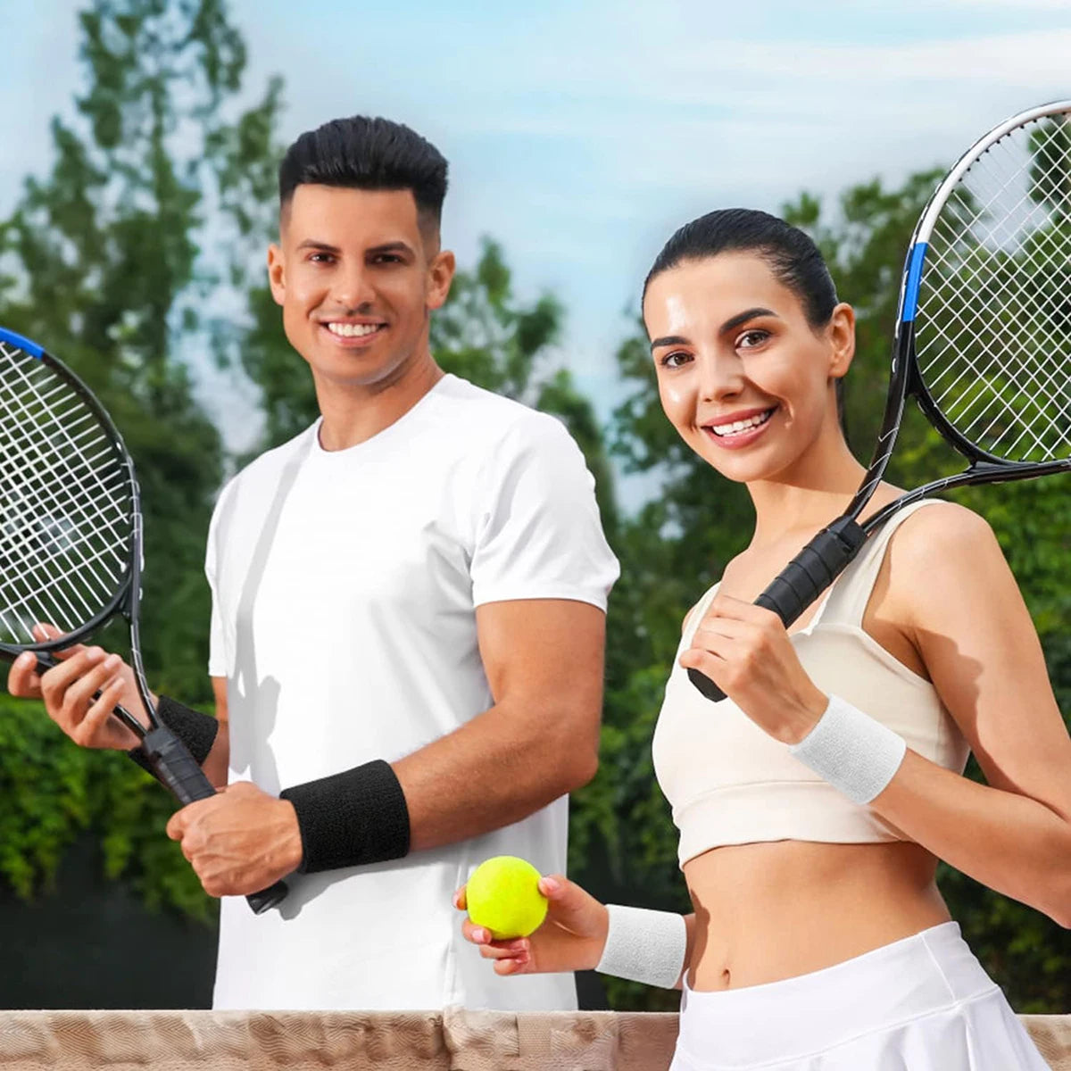 A man and a woman holding tennis rackets and a yellow ball in an outdoor setting.