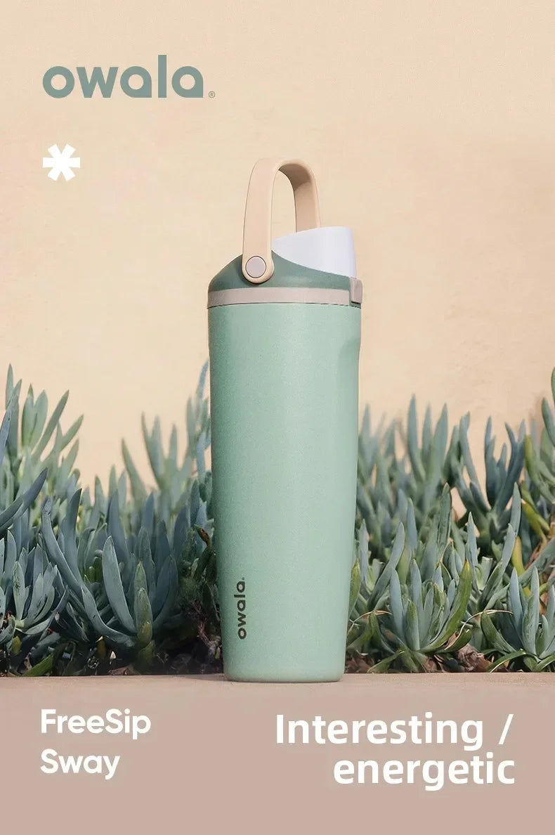 A light green Owala FreeSip Sway insulated travel mug standing in front of green succulent plants.