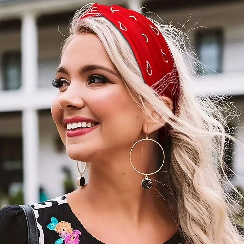 A woman with long blonde hair wears a red bohemian print wide headband and silver hoop earrings.
