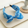 Blue paisley bandana headband tied in a bow displayed on a white tray.