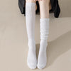 A pair of white slouch knit scrunch socks worn on a person's leg, paired with black clothing.