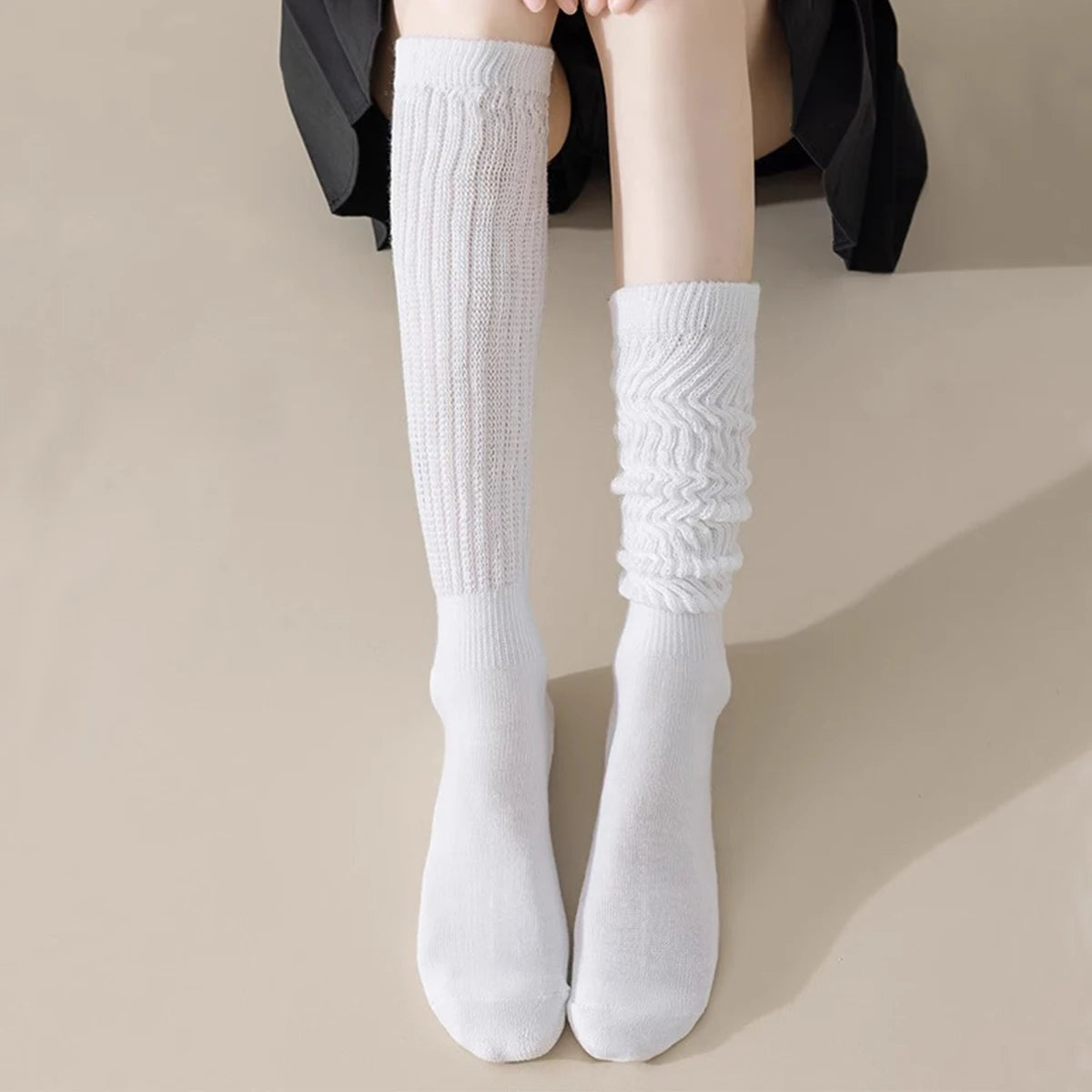 A pair of white slouch knit scrunch socks worn on a person's leg, paired with black clothing.