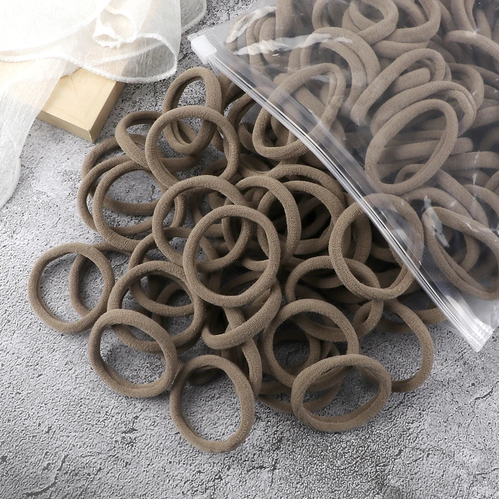 A pile of 50 pieces of mixed color elastic hair bands lying on a gray surface.