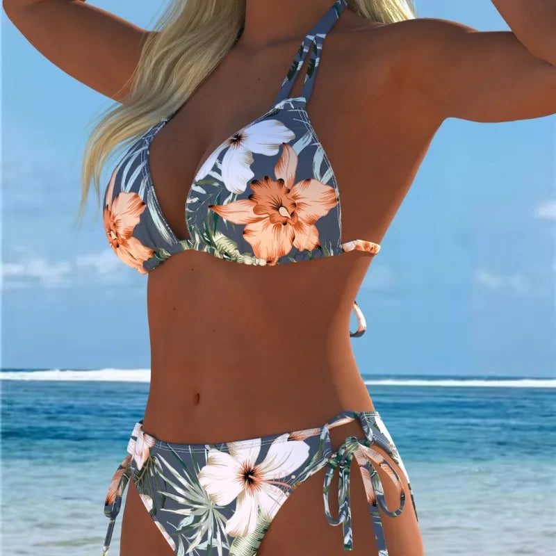 A woman wearing a floral print lace-up two-piece bikini swimsuit standing near the ocean.
