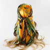 A yellow and green satin square scarf tied around a person's hair, featuring floral and natural patterns.