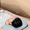 A person is using a light blue inflatable pillow for neck and lumbar support while lying down.