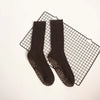 A pair of dark brown mid-calf yoga and pilates socks laid on a black grid surface.