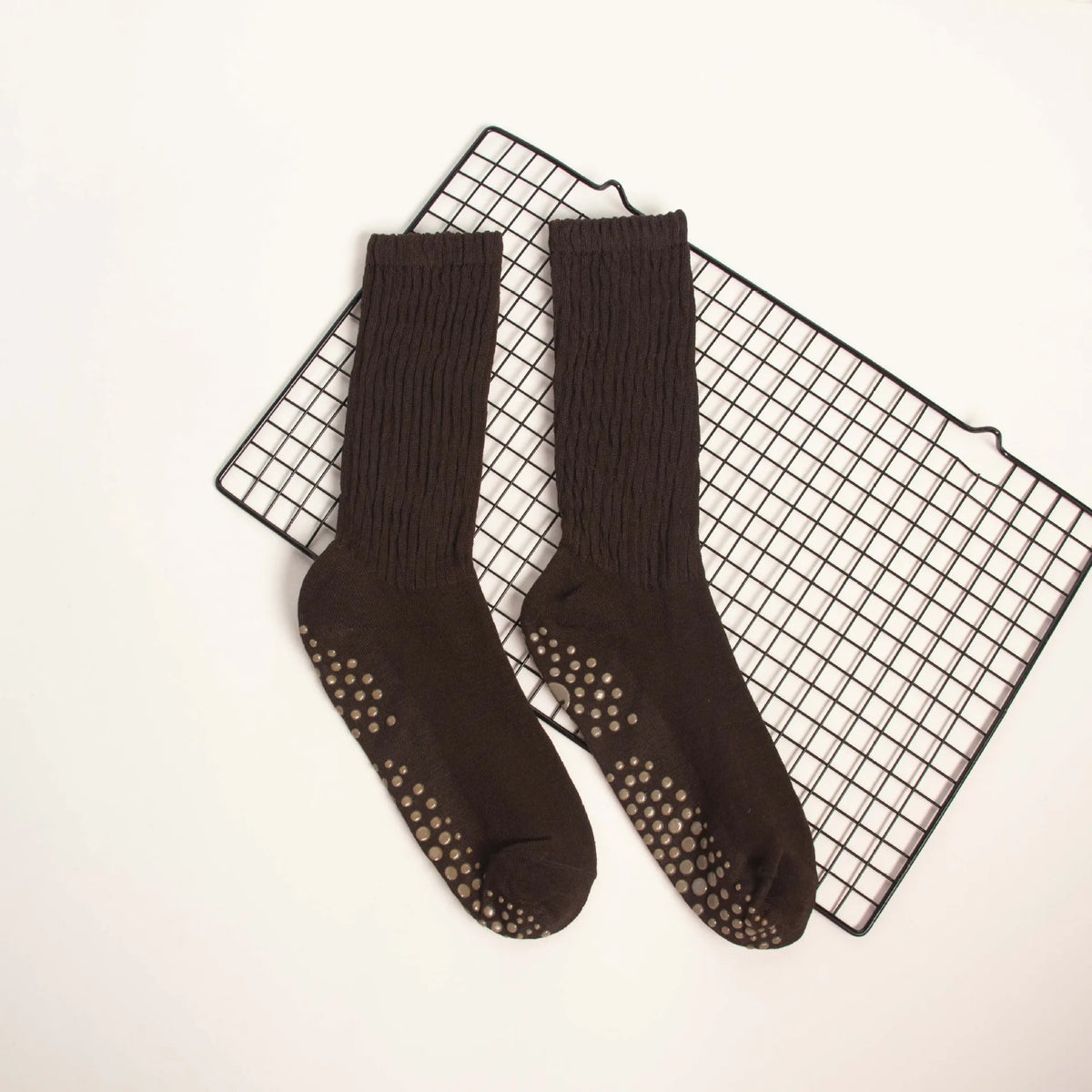 A pair of dark brown mid-calf yoga and pilates socks laid on a black grid surface.
