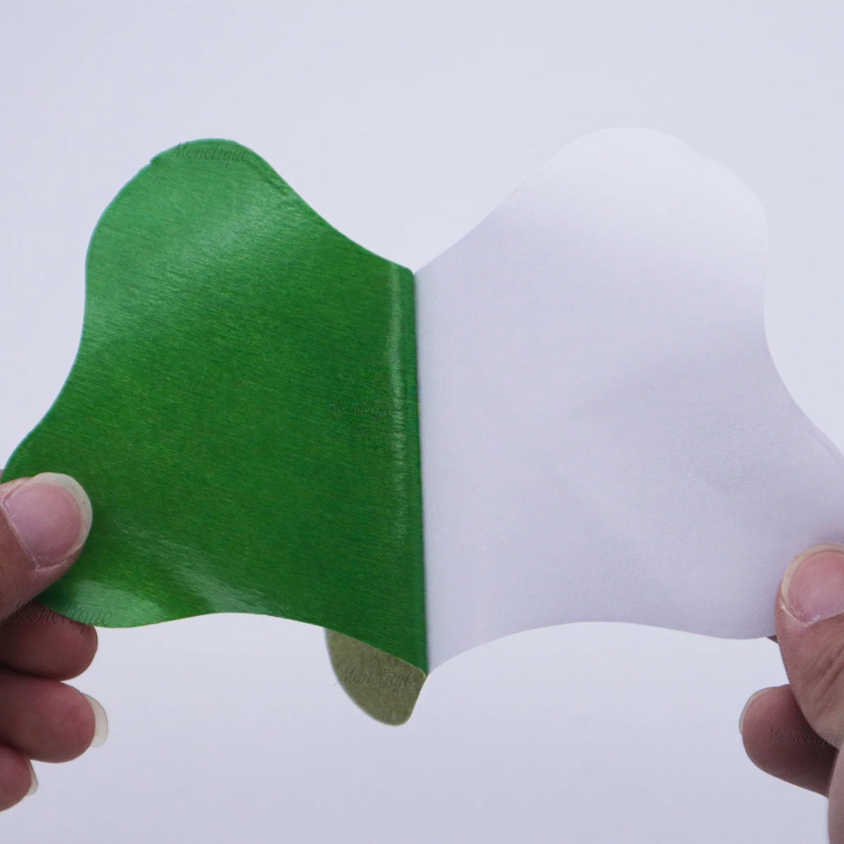 A green and white self-heating lumbar spine patch is held between fingers.