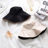 A black double-sided wide brim bucket hat is displayed on white fabric next to a stack of books.