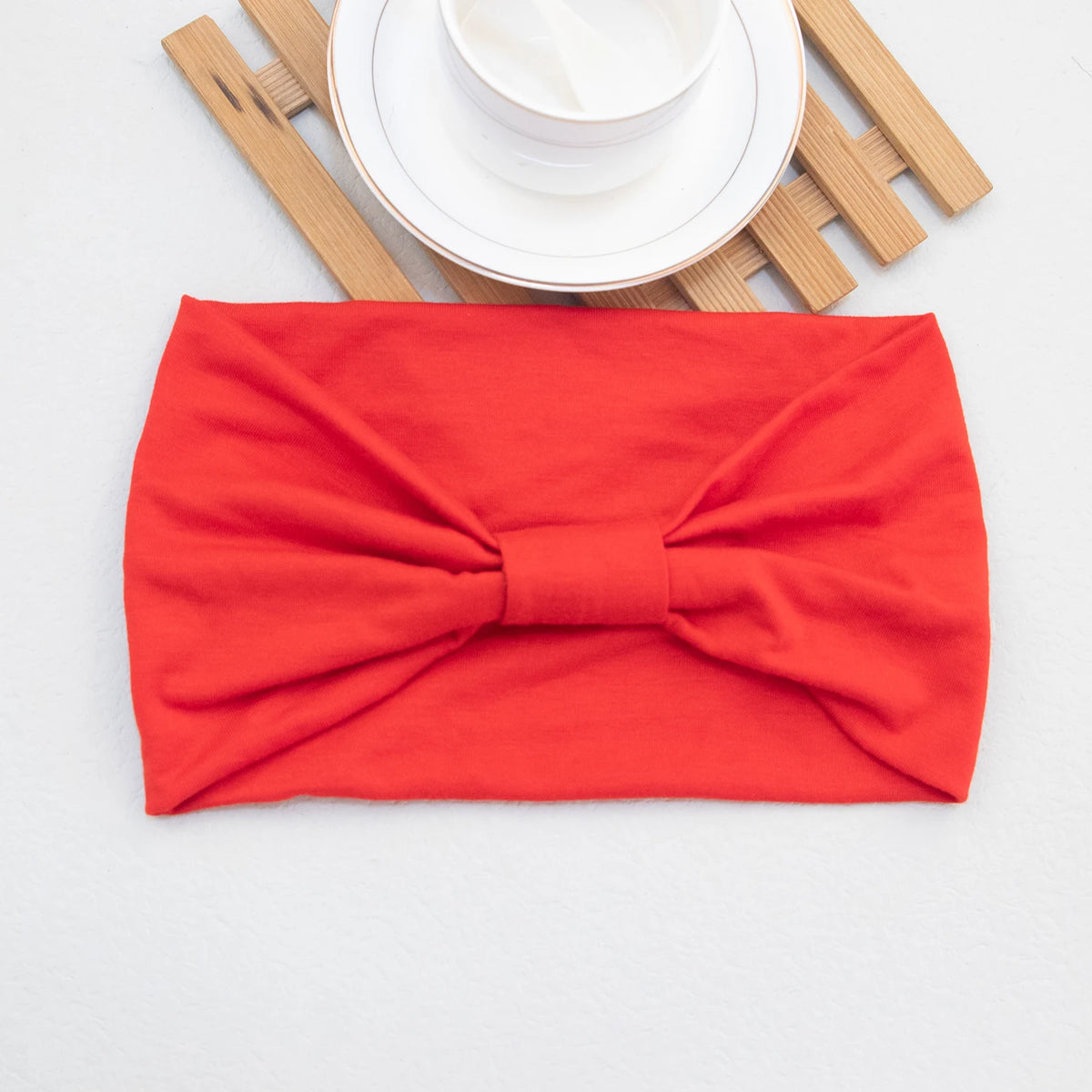 Ein leuchtend rohes Haarband oder Scrunchie neben einer weißen Untertasse und Holzstäbchen.