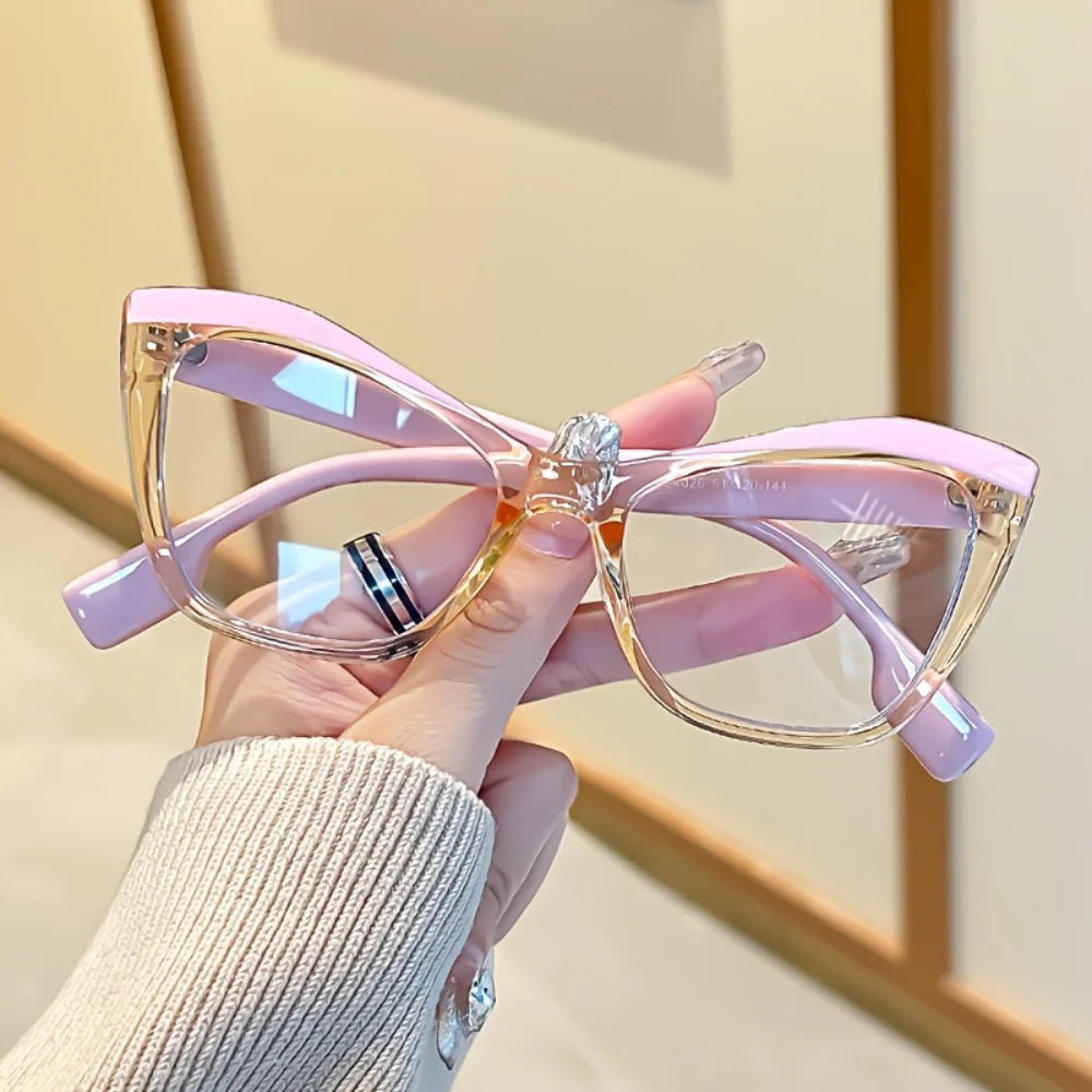 A hand holds a pair of vintage color block blue light blocking eyewear with pink frames.