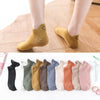 Colección de calcetines tobilleros de varios colores y texturas con caras sonrientes bordadas sobre una superficie blanca.