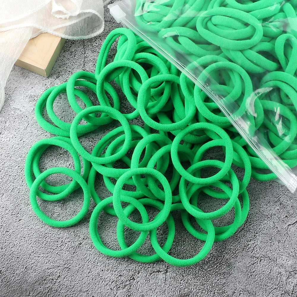 A pile of bright green elastic hair bands, some packaged in clear plastic, resting on a gray surface.