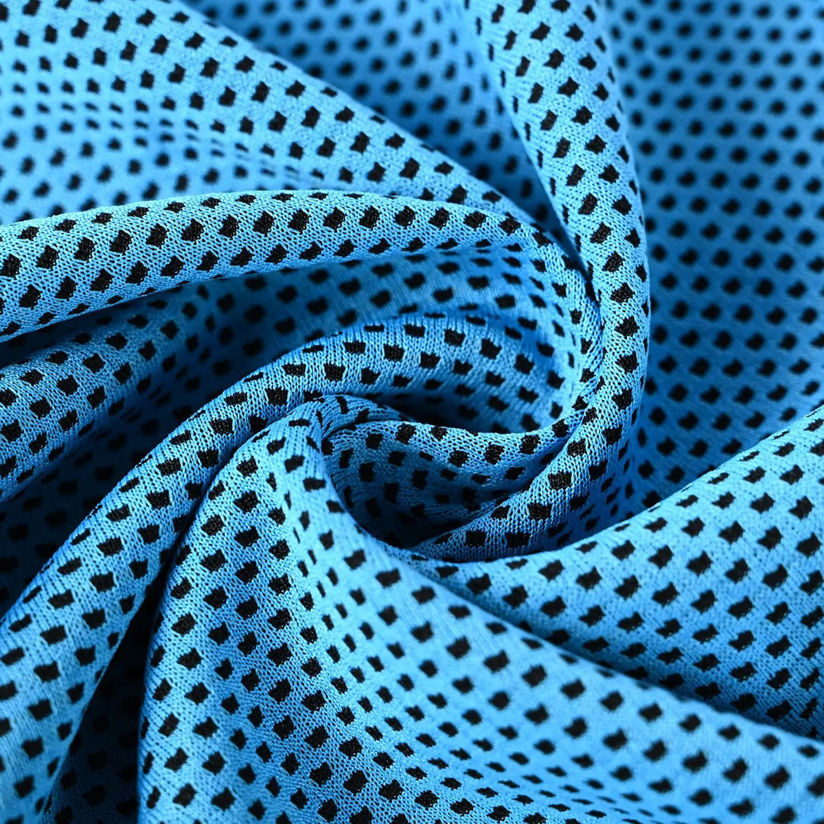 A close-up of a blue microfiber cooling towel fabric folded into a swirl with a black polka dot pattern.
