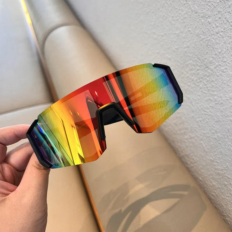 A hand holds a pair of orange and yellow polarized cycling sunglasses against a light background.