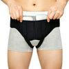 A person is holding an adjustable hernia belt with dual compression pads over light gray shorts.