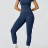 Eine Frau trägt ein dunkelblaues Yoga-Set mit hohen Bund-Leggings und einem kurzärmeligen Oberteil.