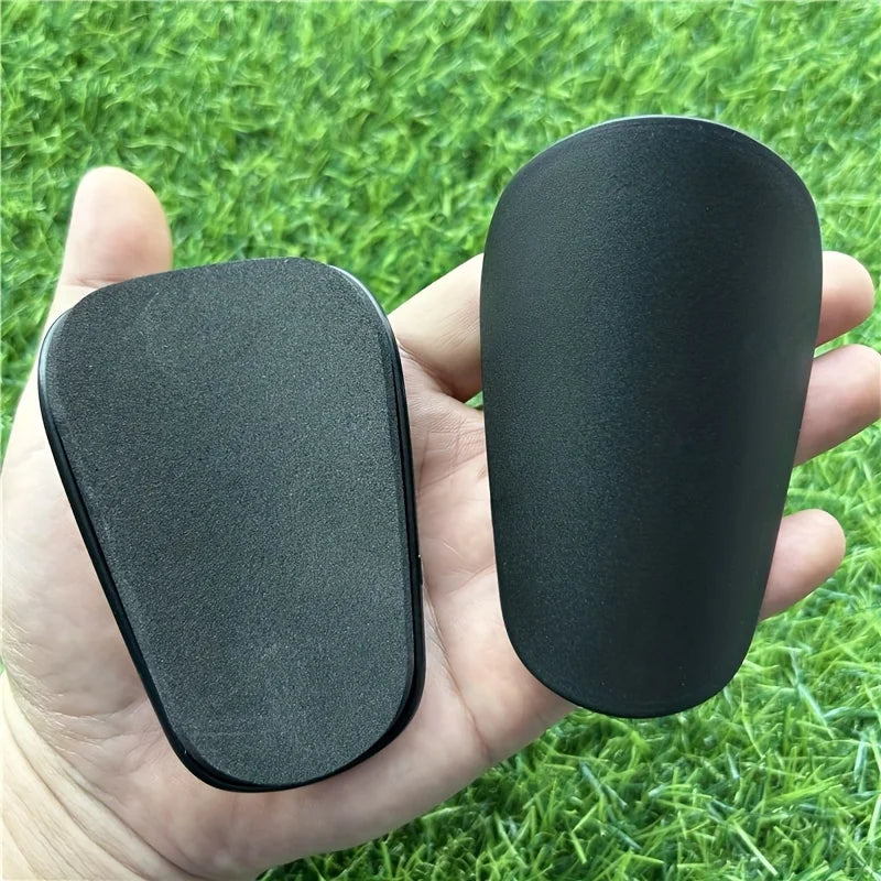 Une main tient une genouillère de soccer noire pour l'entraînement sur de l'herbe verte.