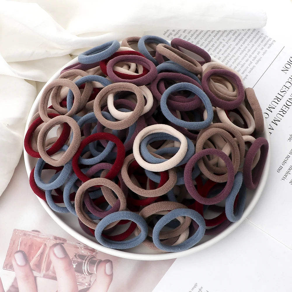 A pile of 50 mixed color elastic hair bands in various shades of brown, red, and blue on a white plate.