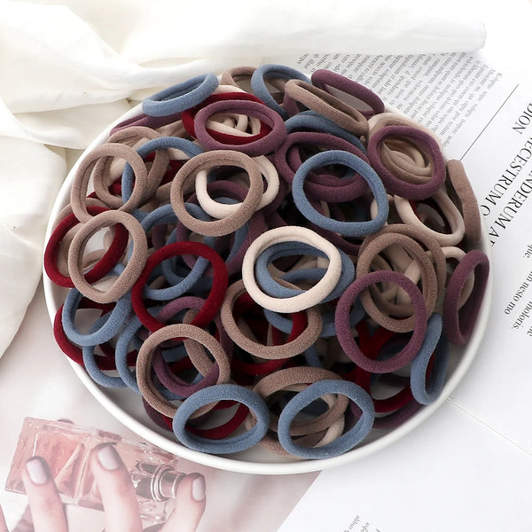 Una pila de 50 bandas elásticas para el cabello de varios colores, tonos marrones, rojos y azules, sobre un plato blanco.