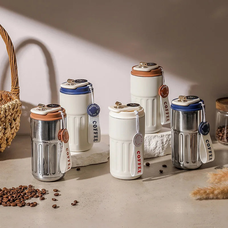 A collection of white and silver insulated thermos bottles with wooden accents sits on a light surface next to coffee beans.