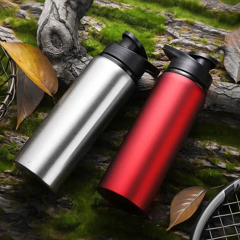 A silver and red leakproof aluminum portable water bottle resting on mossy rocks with leaves.