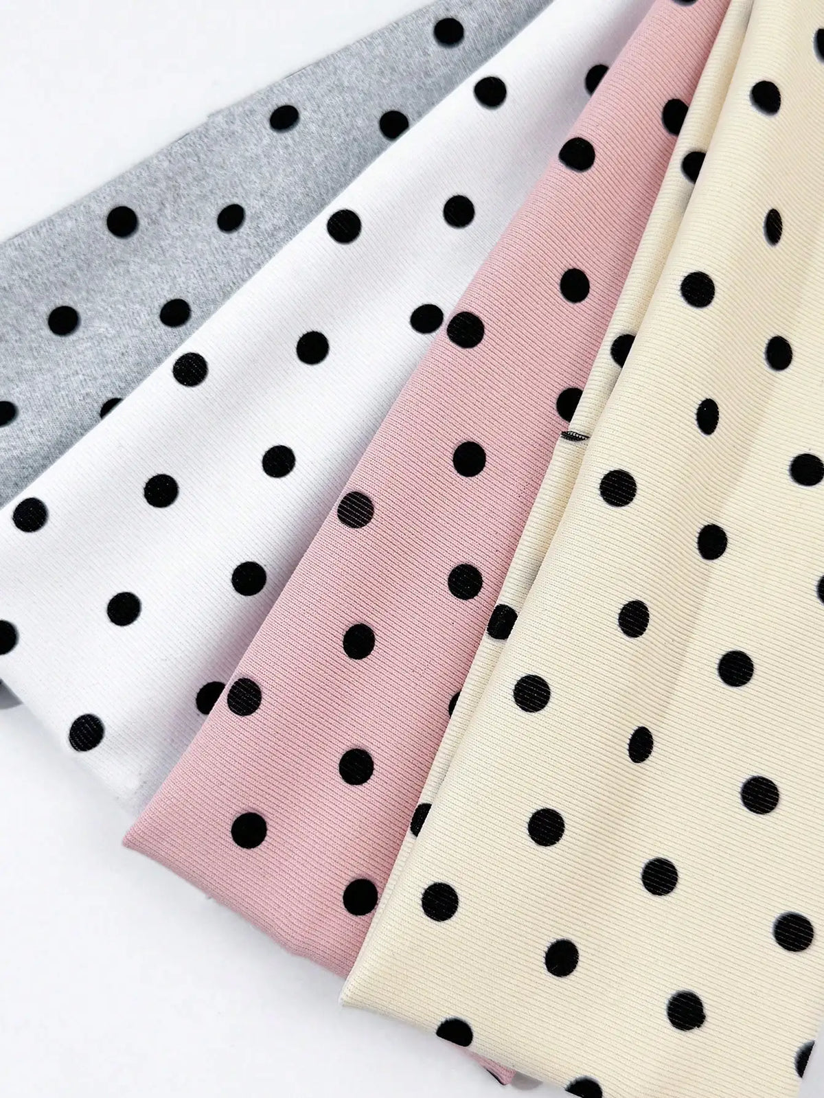 A set of four polka dot elastic hair bands in shades of gray, pink, and cream.