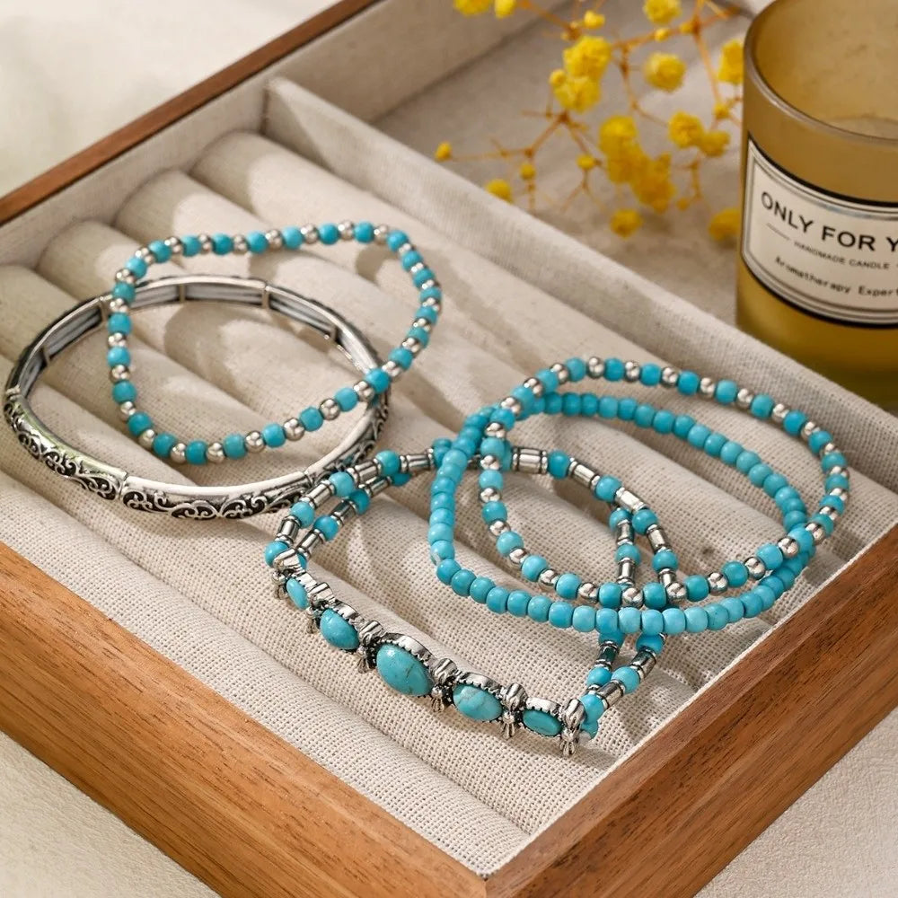 Un set de cinq bracelets en perles turquoise bohèmes, présentés dans une boîte en bois avec une bougie.