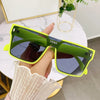 A hand holds a pair of bright lime green oversized square sunglasses with gold accents.