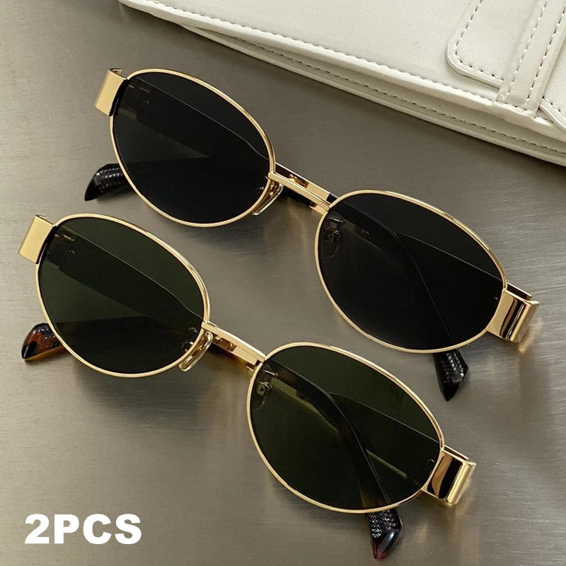 A pair of classic oval metal sunglasses in gold-toned frames with dark lenses resting on a gray surface.