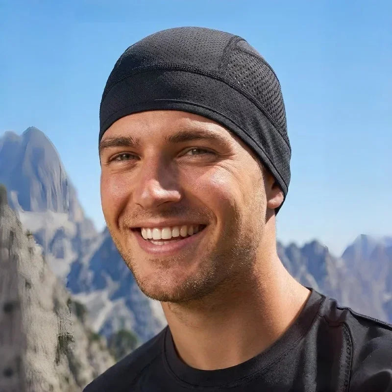 Hombre sonriente con casco de ciclismo negro transpirable y gorra interior, al aire libre con montañas de fondo.