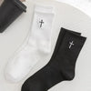 A pair of white and black mid-length cotton socks with a cross design are displayed on a white surface.