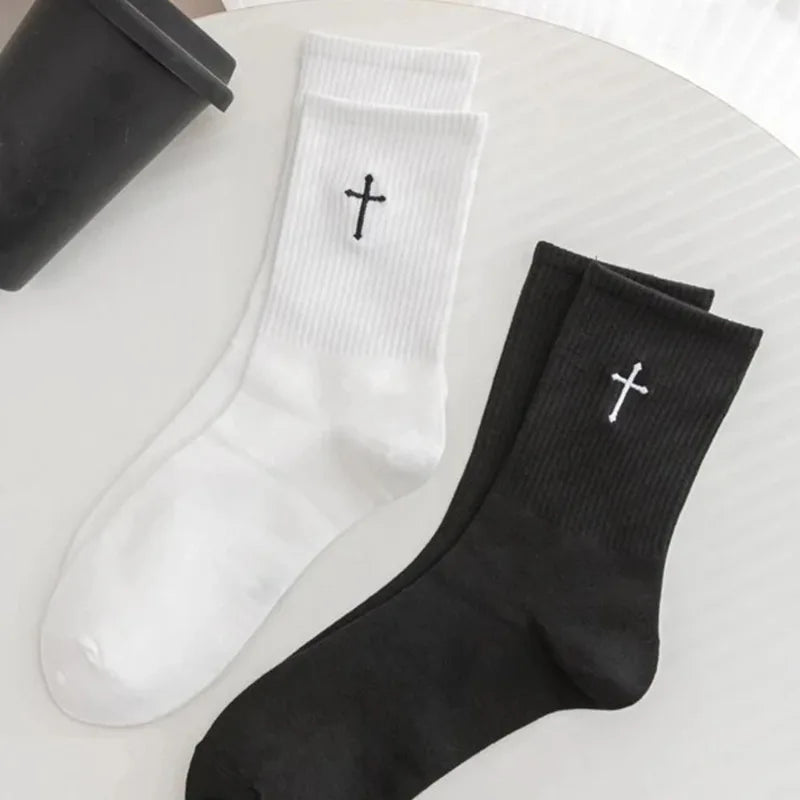 A pair of white and black mid-length cotton socks with a cross design are displayed on a white surface.