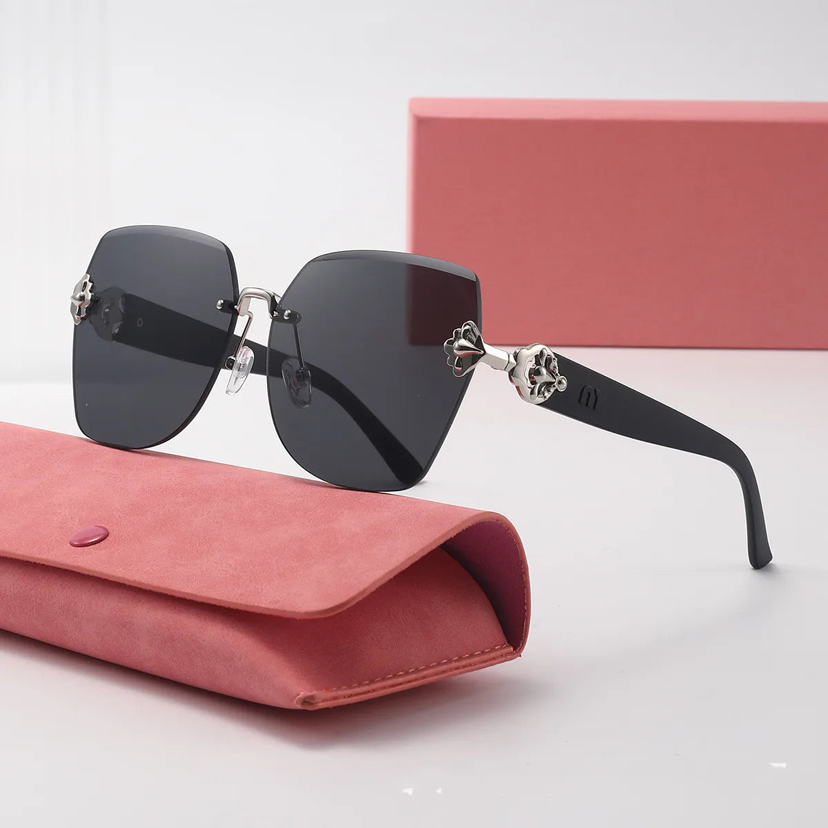 A pair of black frameless sunglasses resting on a pink leather wallet next to a pink box.