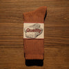 A brown tube sock with a white graphic featuring the word Quality