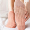 A close-up of a pair of light peach breathable mesh lace tube socks being held by a hand.