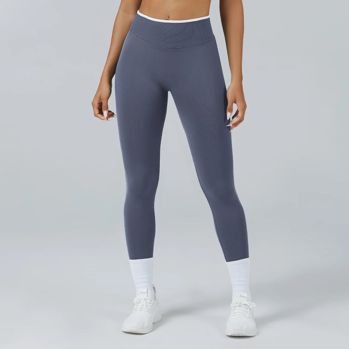 A woman wearing dark gray high-waist yoga leggings and white socks standing against a light background.