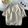 Beige, überdimensioniertes Baumwoll-T-Shirt einer Frau auf weißem Plüsch neben einem Teddybär und Sonnenbrille.