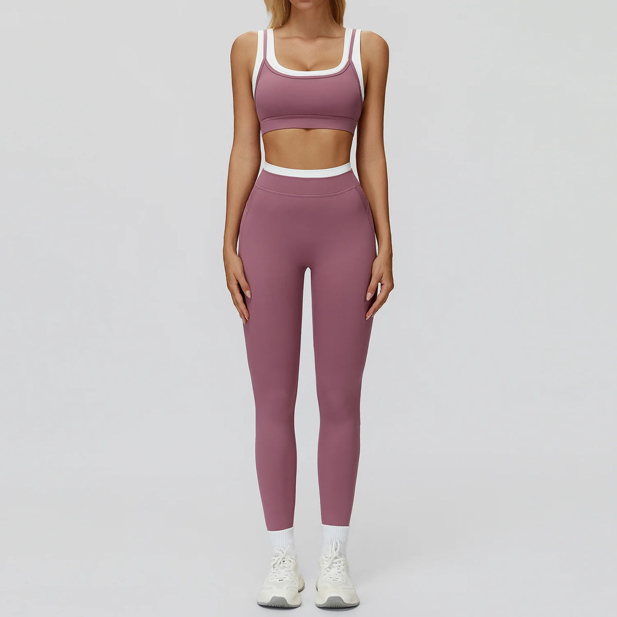 Eine Frau trägt ein zweiteiliges mauve Yoga- und Trainingsanzugset mit croppedem Oberteil und passenden Leggings.