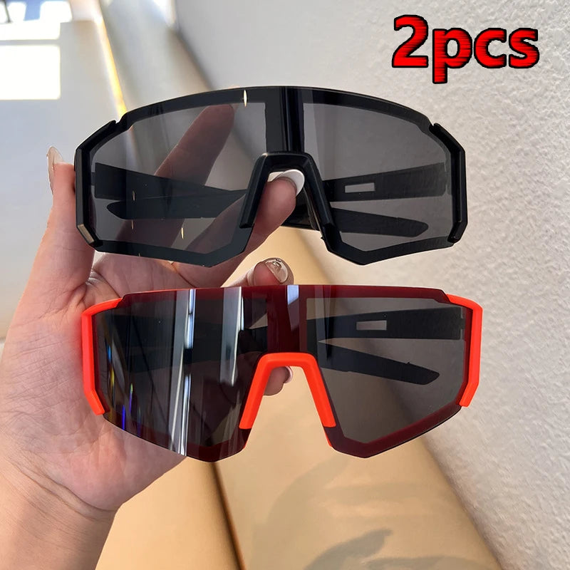 A hand holds two pairs of black and red cycling sunglasses for outdoor sports.