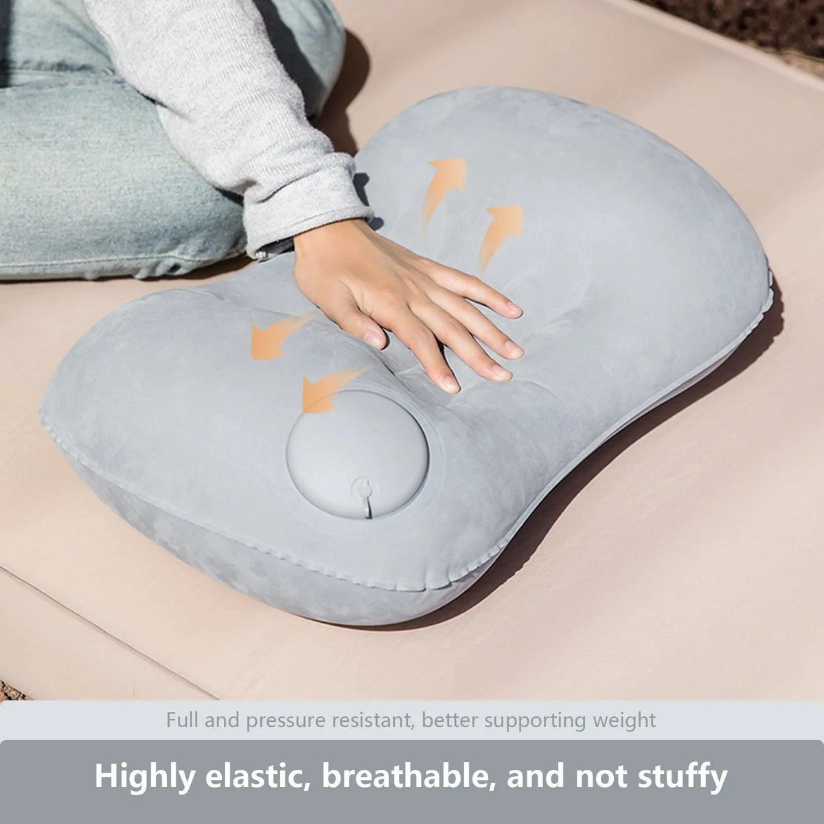 A gray inflatable camping pillow is shown being used for neck and lumbar support on a tan surface.